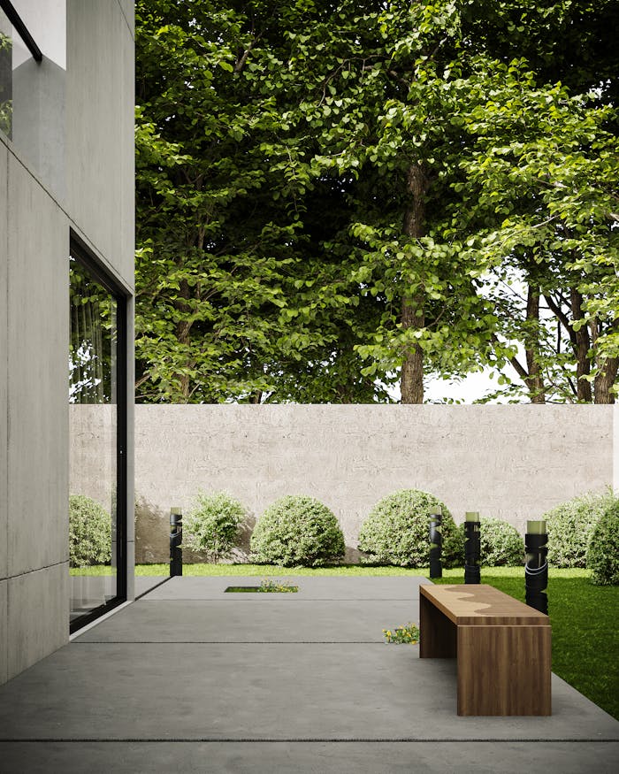 A minimalist outdoor concrete patio with a wooden bench and green garden backdrop.